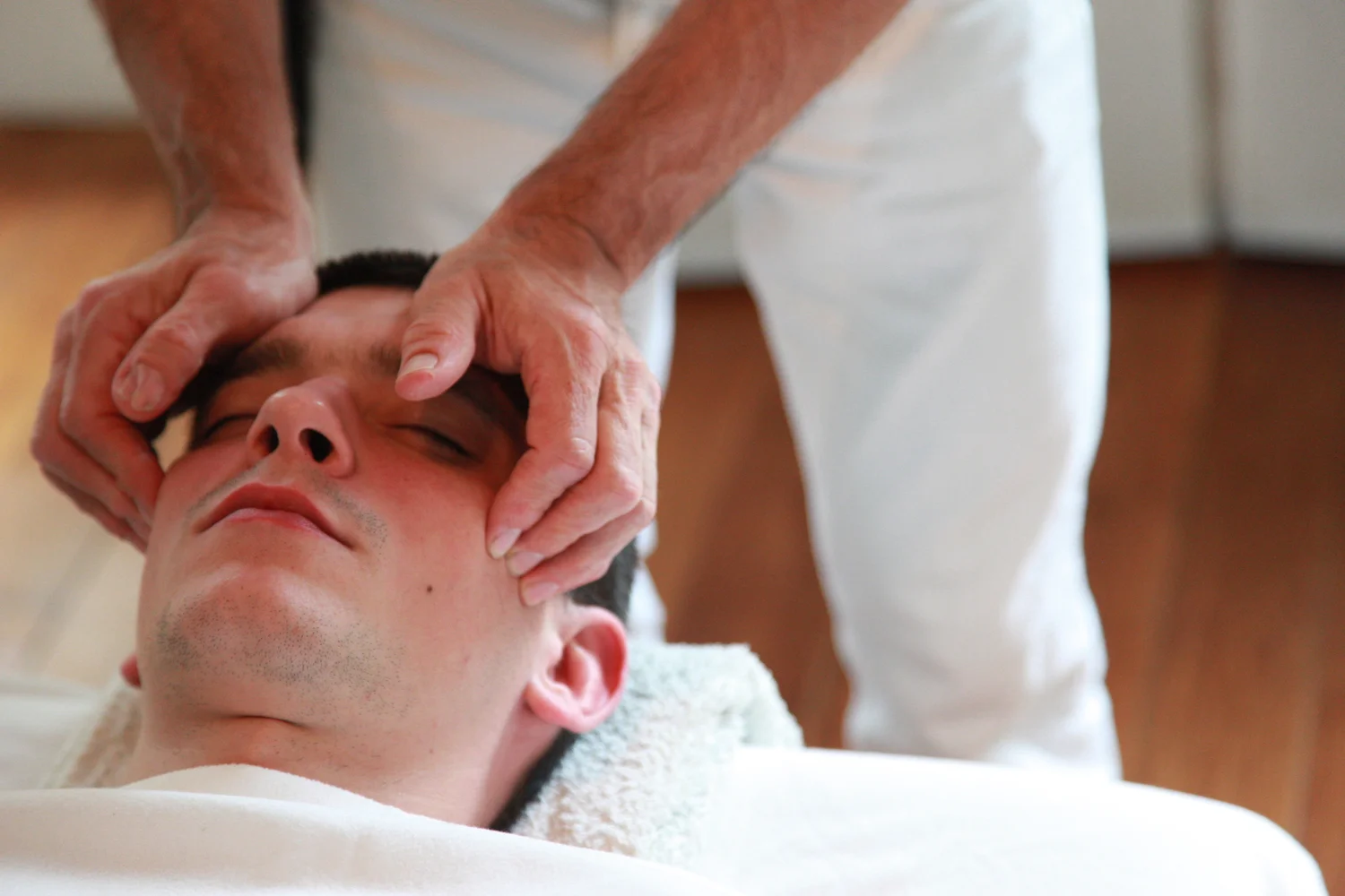 Mains pos&eacute;es sur le visage d&rsquo;une personne allong&eacute;e pendant une s&eacute;ance en cabinet